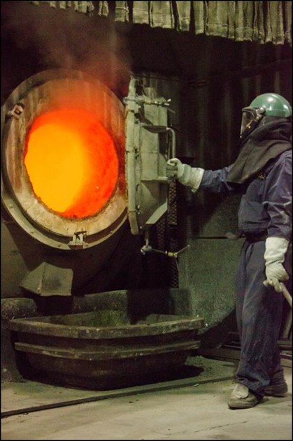 A worker in protective gear opening the door to a glowing red furnace