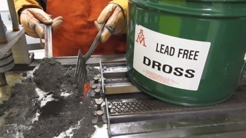 A worker scooping dross from a solder pot into a reclaim bucket